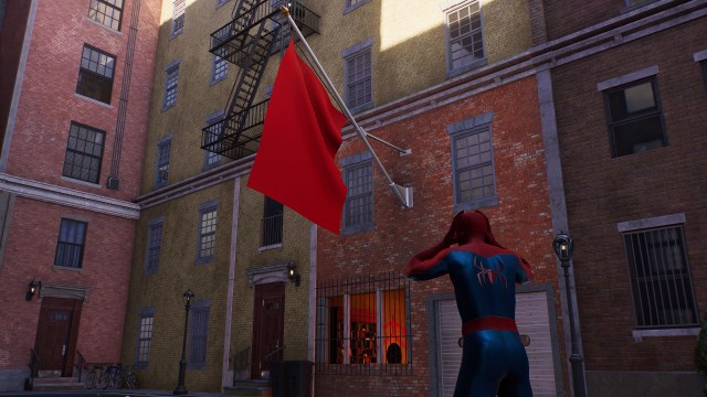Spider-Man holds his hands on his head while looking at a building with an ominous red flag outside.
